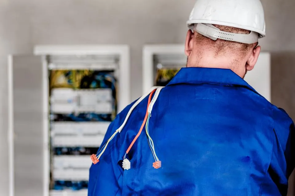Een elektricien in blauwe werkkledij aan een zekeringkast