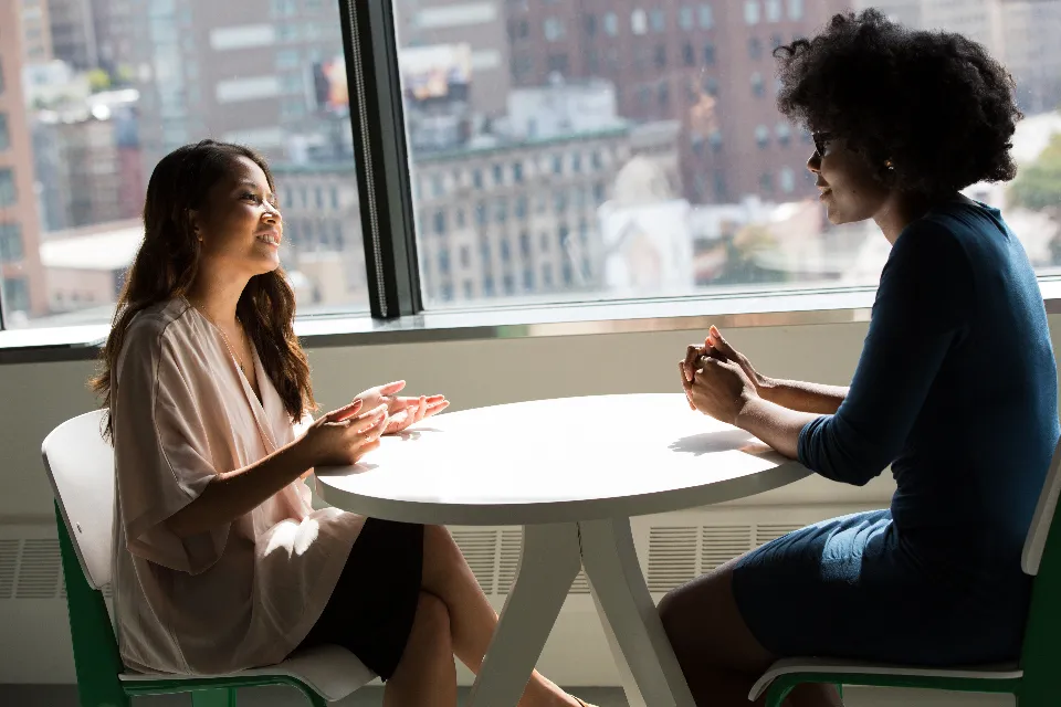 Twee mensen in gesprek aan een tafel bij het raam